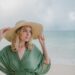 tranquil woman in straw hat on sandy beach near sea
